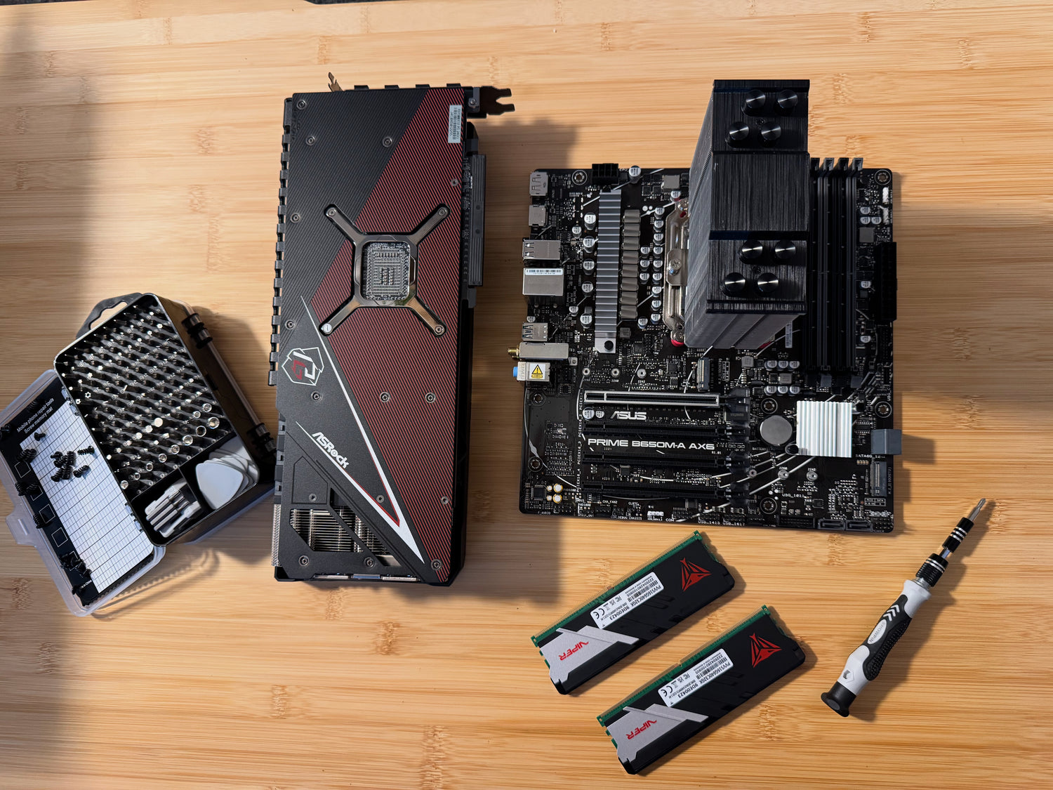 Computer hardware components including a graphics card, motherboard, RAM, and a screwdriver on a wooden surface.